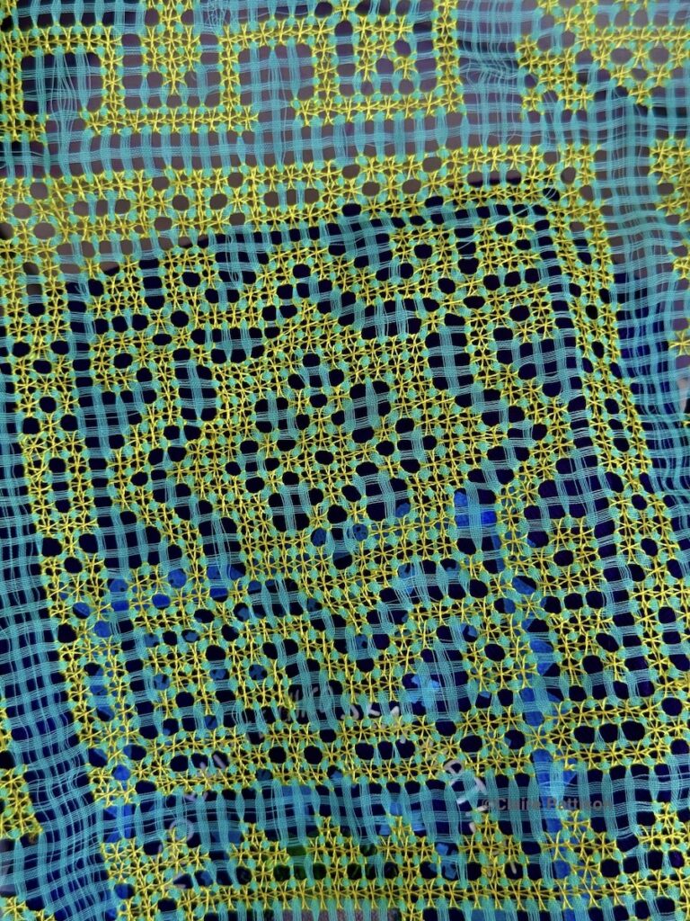 close up of labirinto worked with yellow threads on a blue/green background