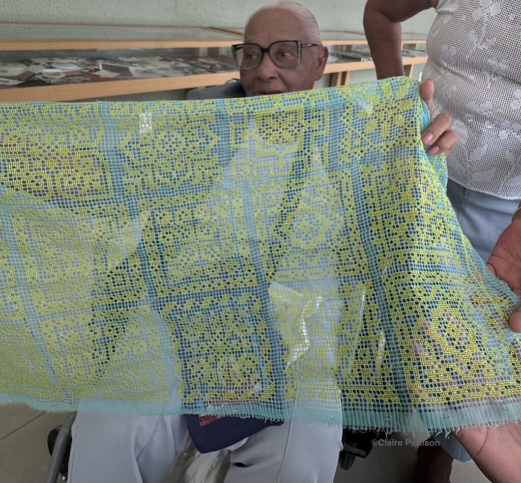 A woman holding a delicate example of her labirinto work with yellow stitches on a green background