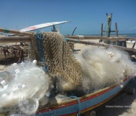 Redes de pesca enroladas e secando ao sol em um barco na praia.