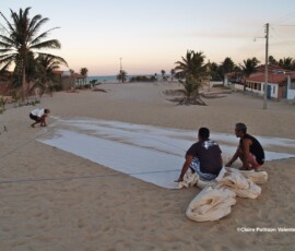 Homens estendendo tecido na areia para cortar uma nova vela.